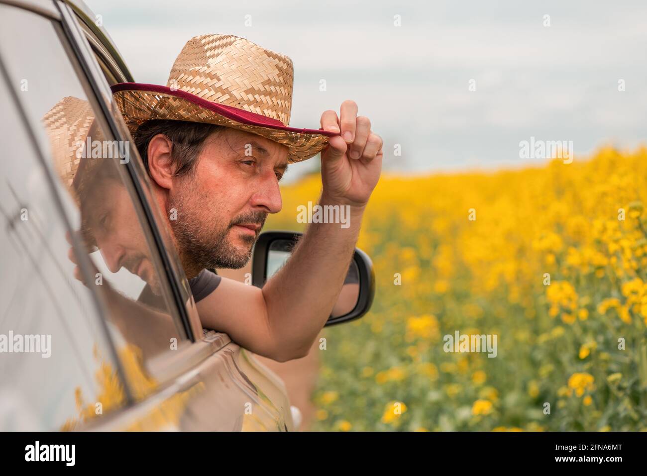 Mann, der in der blühenden Sommerlandschaft Autofahren genießt, Kopf mit Strohhut, der aus dem Fenster reicht, selektiver Fokus Stockfoto