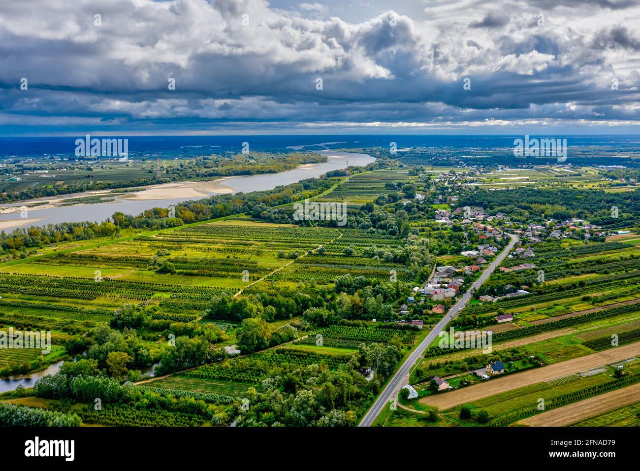 Landschaftlich reizvolle Landschaft, Dorf an gerader Straße und fernem Fluss unter launisch bewölktem Himmel Stockfoto