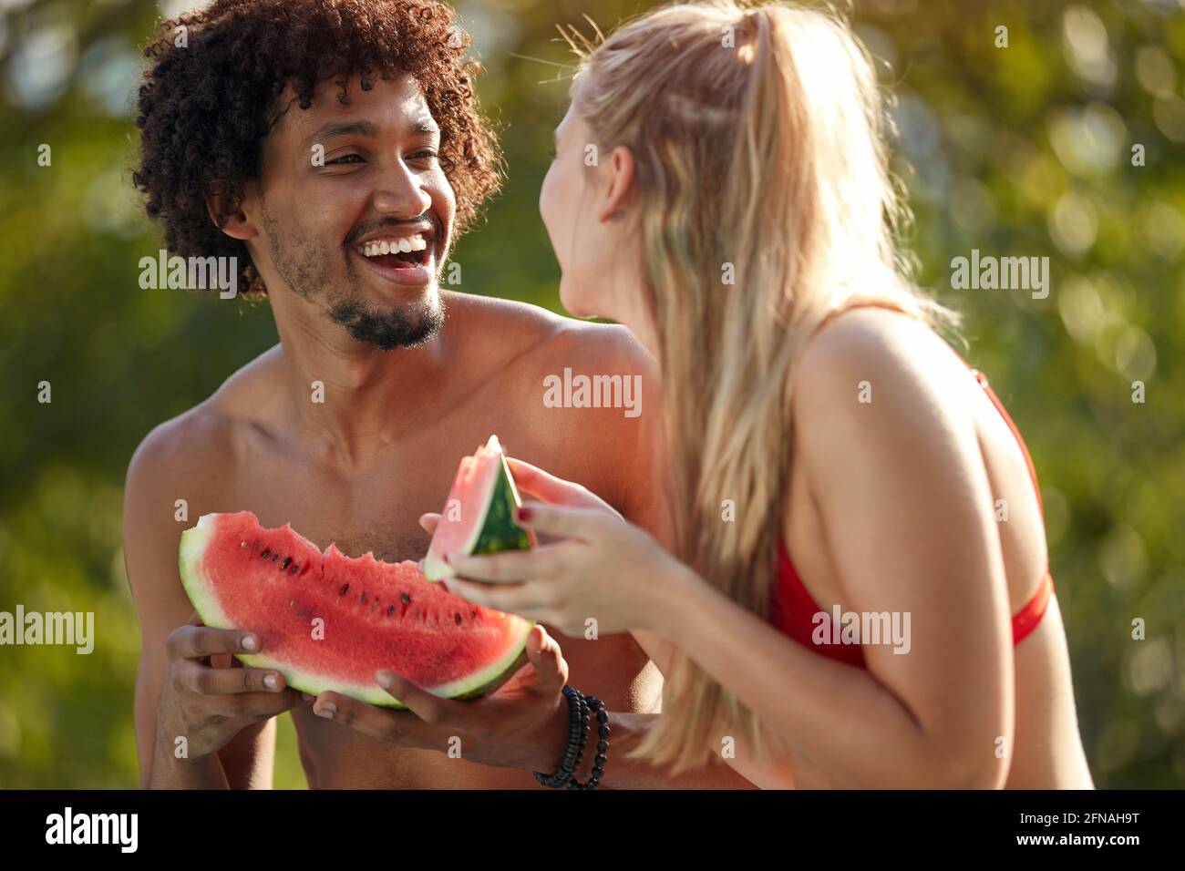 Junge multiethnische Paare schauen sich gegenseitig, lächeln, lachen, während sie Wassermelone essen Stockfoto