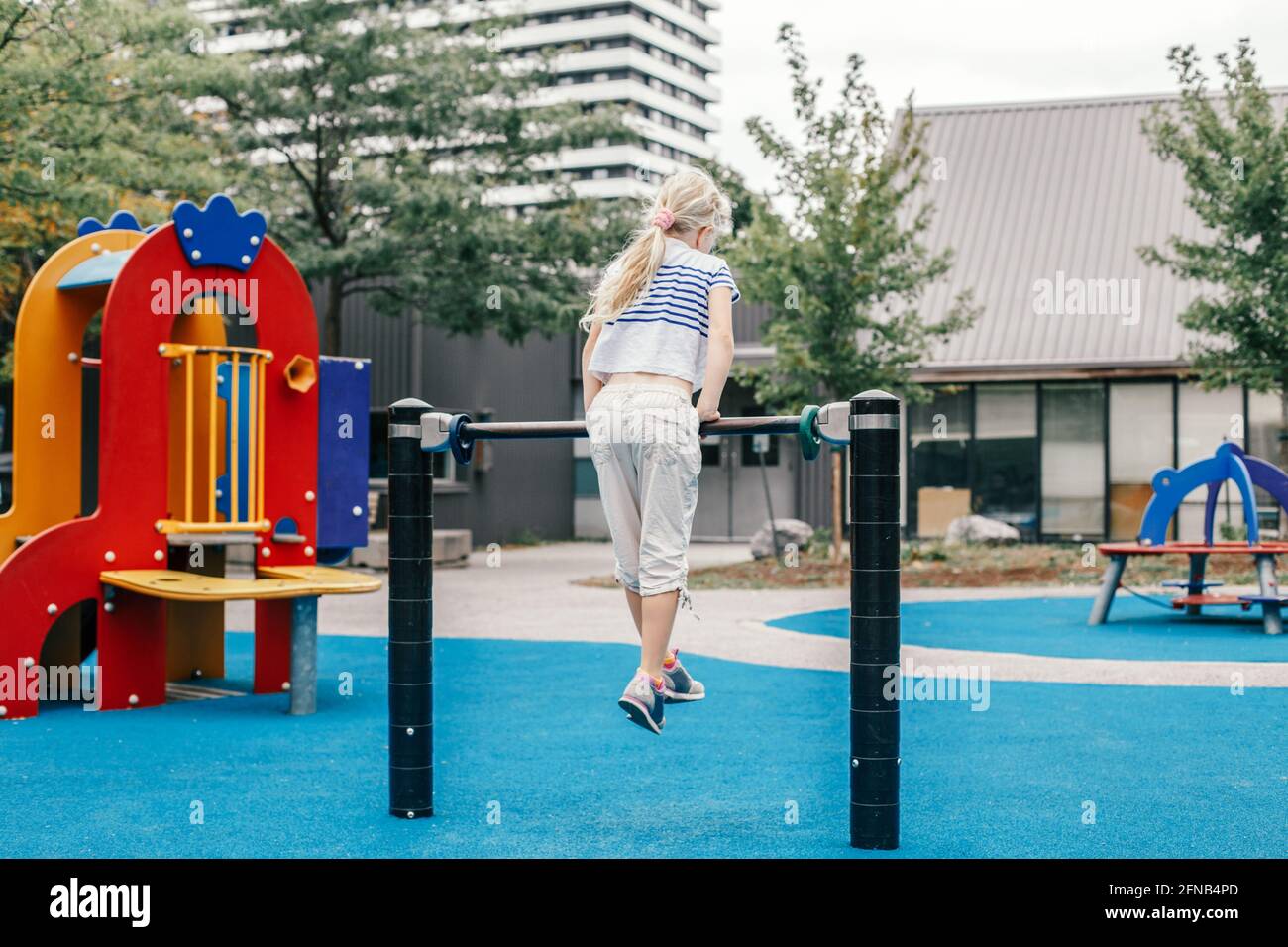 Glücklich lächelndes junges Mädchen, das an der Pull-Ups-Bar für Kinder draußen auf dem Spielplatz trainiert. Kind hängt an der hohen Theke. Sommerspaß, Aktivitätstraining und Fitness Stockfoto