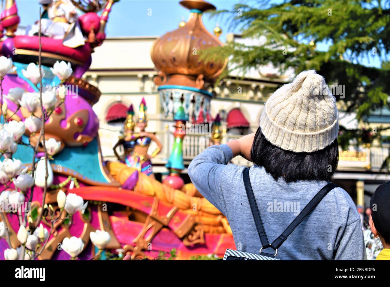 Ein kleines Mädchen in einem Häkelhut sieht sich eine bunte Parade in einem Freizeitpark an Stockfoto