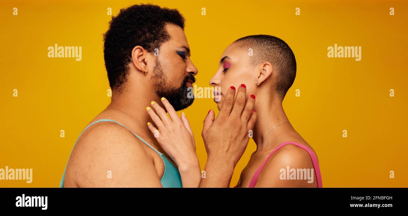 Zärtliches, flüssiges Paar. Nicht binäre männliche und weibliche Personen berühren sich mit geschlossenen Augen auf gelbem Hintergrund. Stockfoto