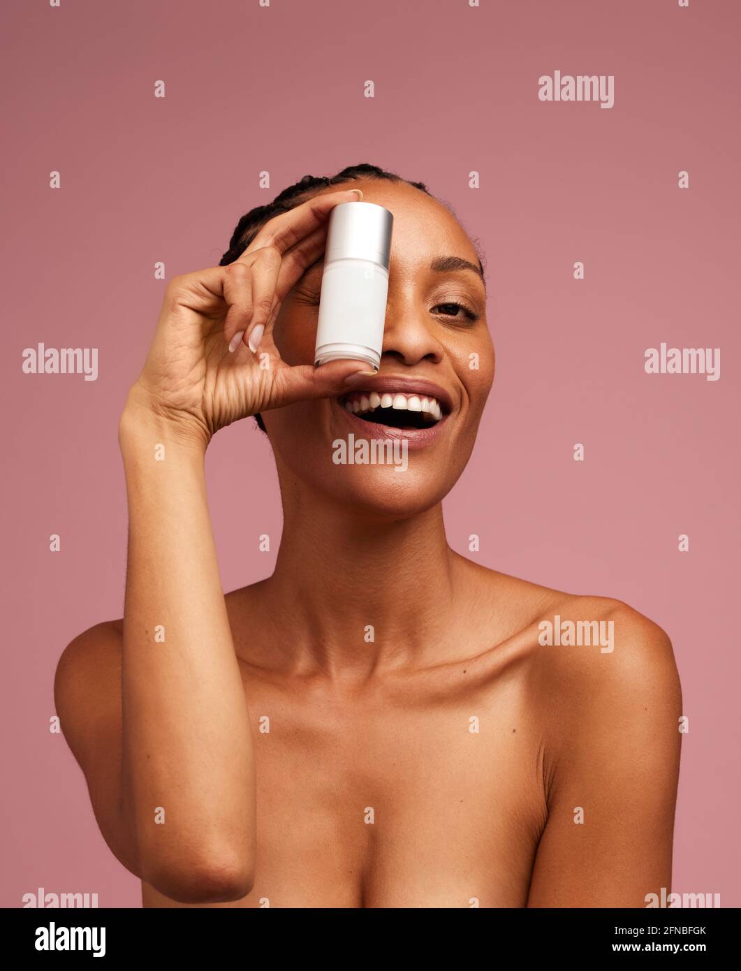 Frau, die eine Hautpflegecreme vor ihrem Auge hält und lächelt. afroamerikanische Frau mit Gesichtscreme vor rosa Hintergrund. Stockfoto