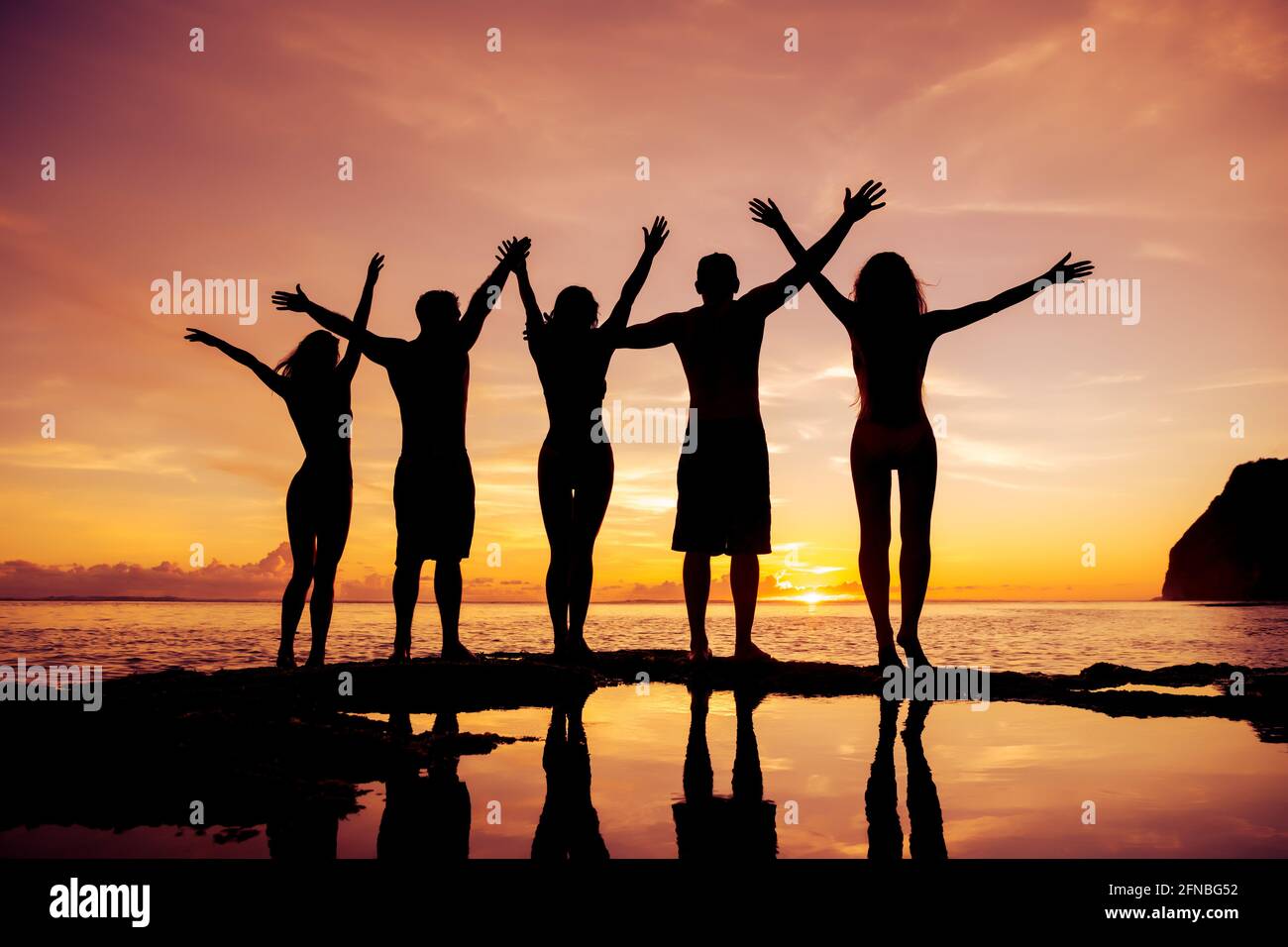 Fünf glückliche junge Freunde stehen mit erhobenen Armen an Strand und genießt den Sonnenuntergang Stockfoto