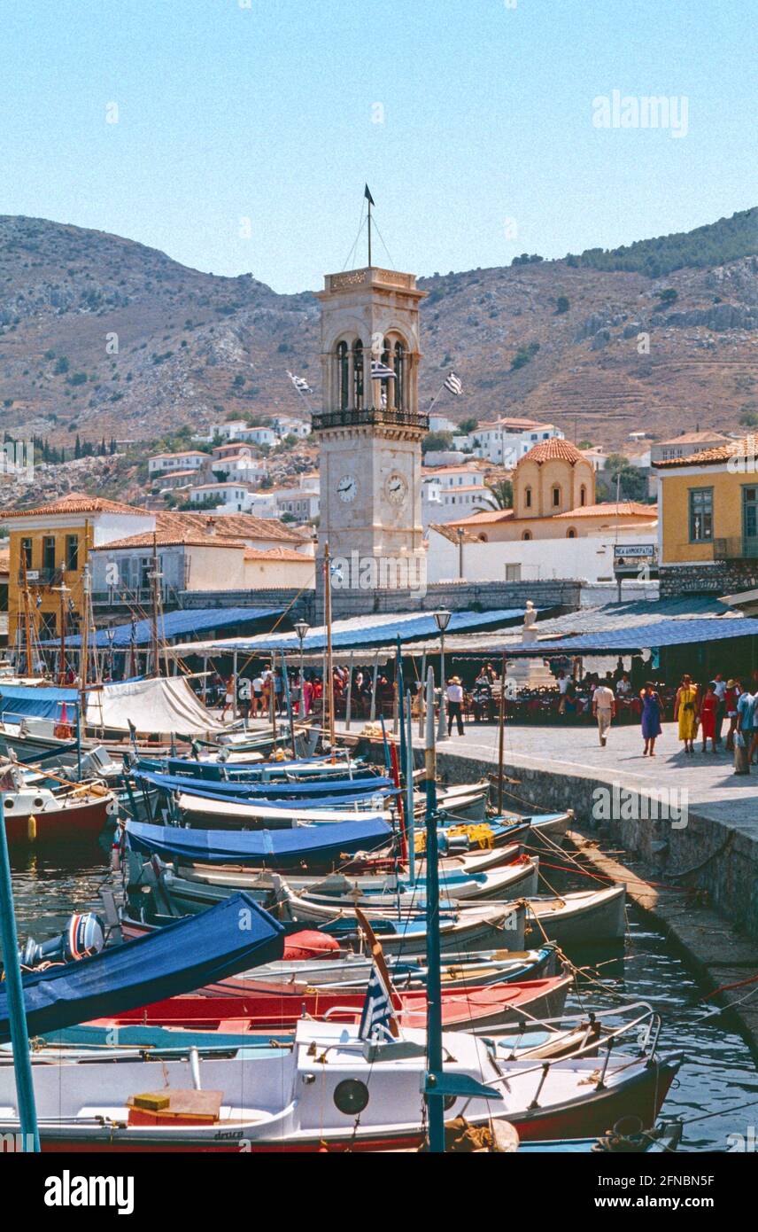 Gescanntes Bild der anliegeten Boote im Hafen einer unberührten Hydra in Griechenland um 1977. Der Uhrturm ist Mittelrahmen und Besucher auf dem Prome Stockfoto