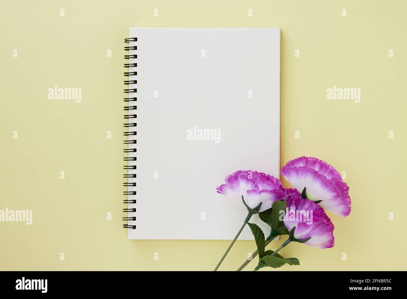 Spiral Notizbuch oder Spring Notizbuch in Unlined Type und Violet Flower auf Pastellgelb minimalistischem Hintergrund. Spiral Notebook Mock up auf Mittelrahmen Stockfoto