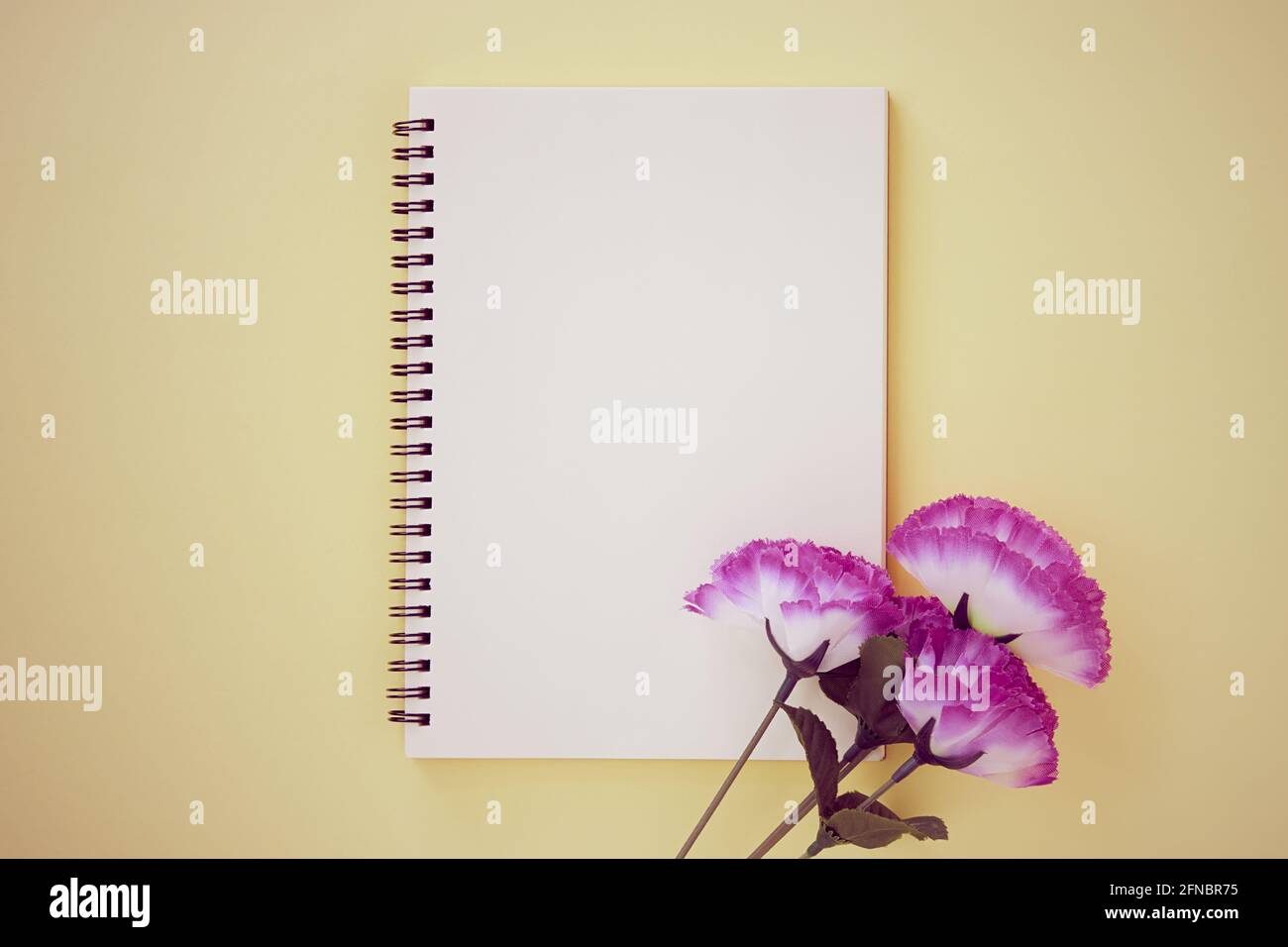 Spiral Notizbuch oder Spring Notizbuch in Unlined Type und Violet Flower auf Pastellgelb minimalistischem Hintergrund. Spiral Notebook Mock up auf Mittelrahmen i Stockfoto