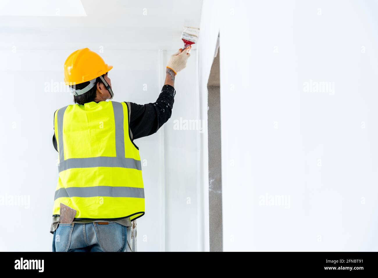 Nahaufnahme Maler Mann Malerei die Wand in einem unfertigen Gebäude, mit Pinsel, isoliert auf großen leeren Raum mit Holzleiter an der Konstruktion Stockfoto