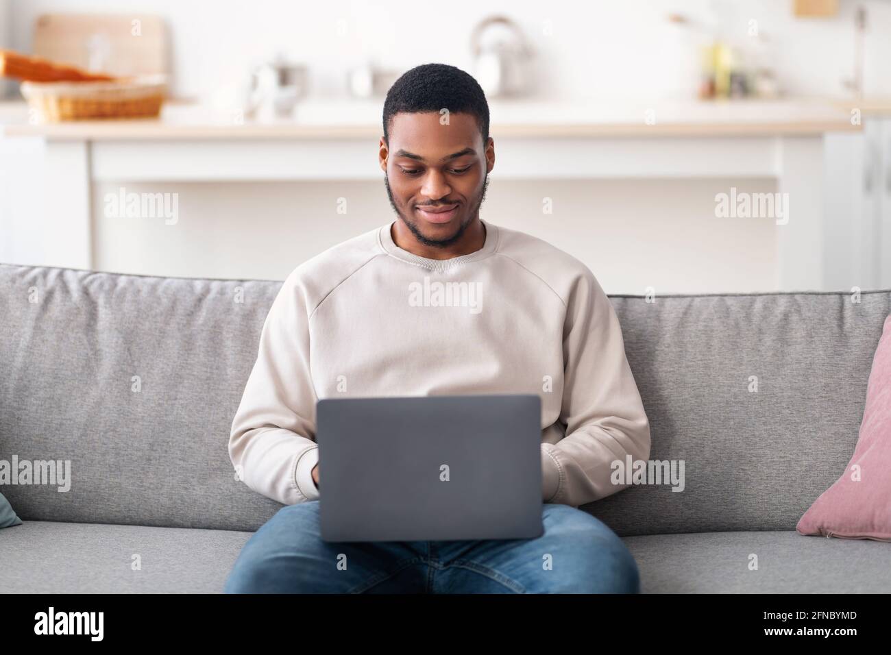Lächelnder schwarzer Mann, der einen Laptop benutzt und auf dem Sofa sitzt Stockfoto