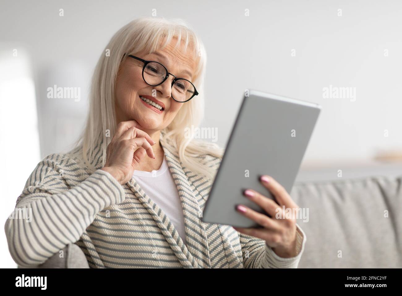 Lächelnde reife Frau mit Tablet auf der Couch sitzen Stockfoto