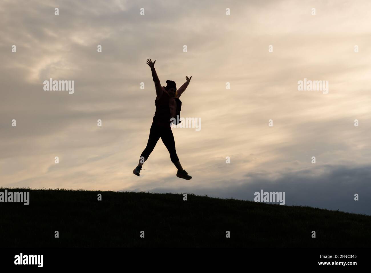 Silhouette einer sportlichen Frau, die bei Sonnenuntergang auf einem Hügel in die Luft springt. Sternpose. Konzept von Glück, feierliche Energie. Stockfoto