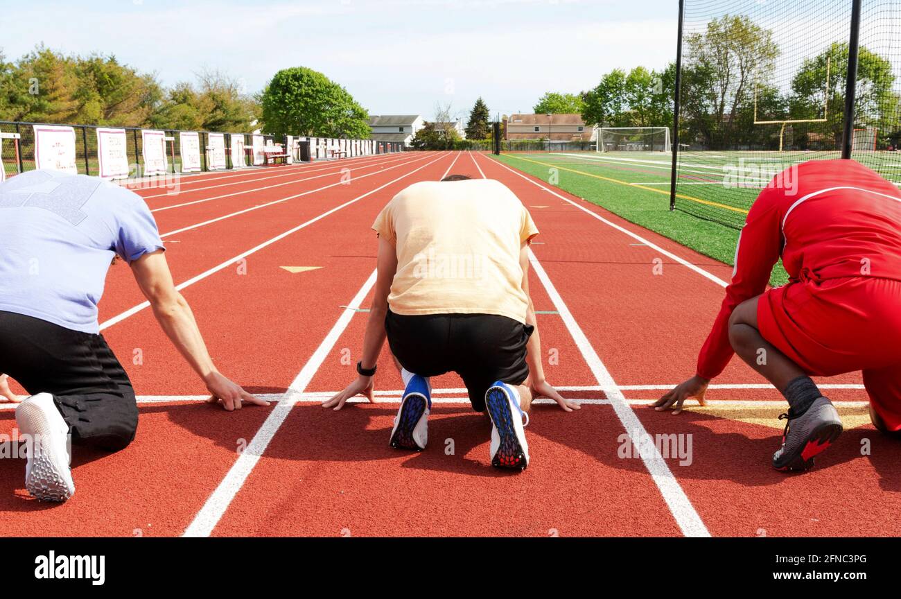 Rückansicht von drei männlichen High School Sprinterläufern, die beim Training auf der Strecke an der Startlinie bereit waren. Stockfoto