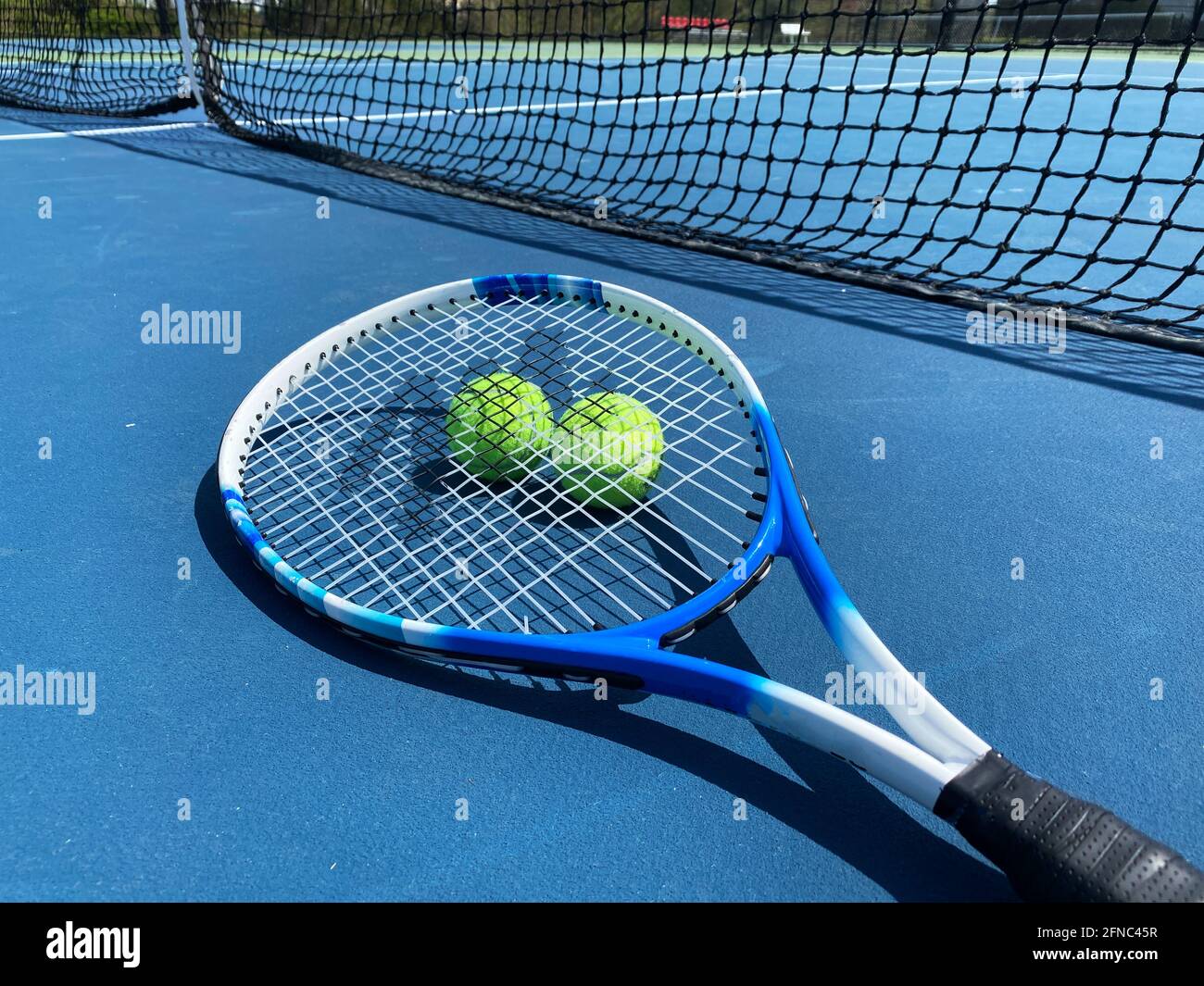Ein Tennisschläger auf dem Boden mit zwei Kugeln unter Der Schläger auf einem blauen Platz vor dem Netto Stockfoto