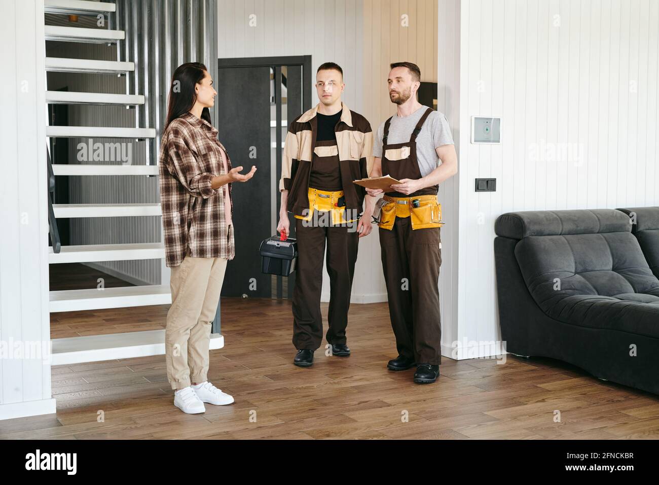 Zwei Klempner und eine junge Frau unterhalten sich über Probleme mit der Wasserleitung Im Wohnzimmer Stockfoto