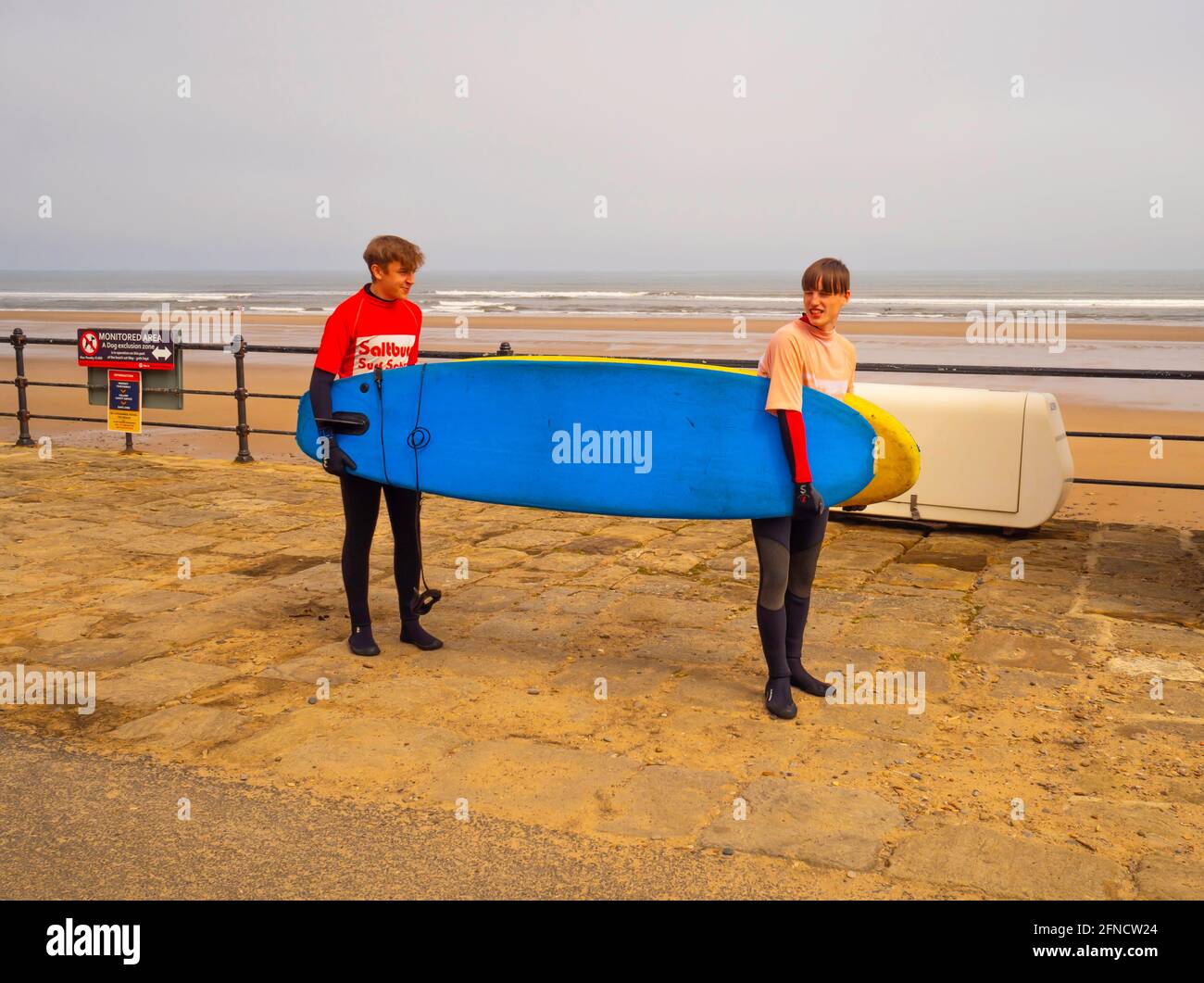 Zwei junge Männer, die Surfbretter zum Meer tragen Die Saltburn Surf School Stockfoto
