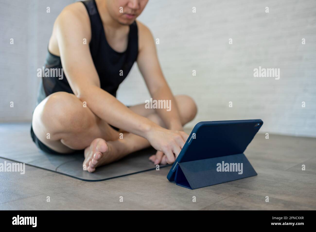 Junger asiatischer Mann, der zu Hause trainiert, während er sich ein Video-Tutorial auf dem Tablet ansieht. Männlich Fitness guy Training drinnen online Stockfoto