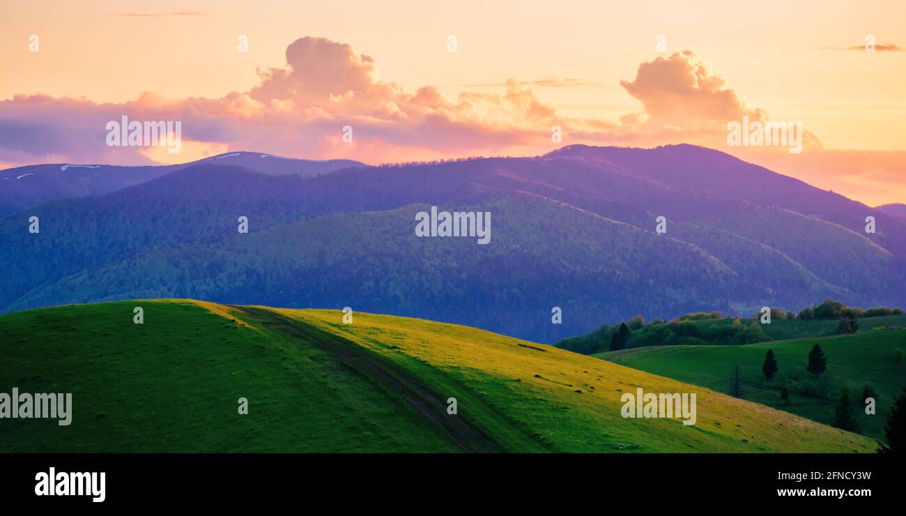 Hügelige ländliche Berglandschaft in der Dämmerung. Wunderschöne Naturkulisse im Frühling. Wolken am Himmel im Abendlicht Stockfoto