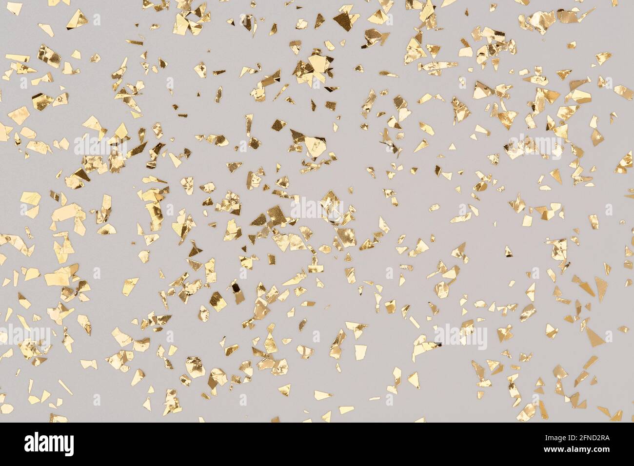 Goldenes Konfetti auf grauem Hintergrund, Glitzerhintergrund aus Party-Goldfolie. Stockfoto