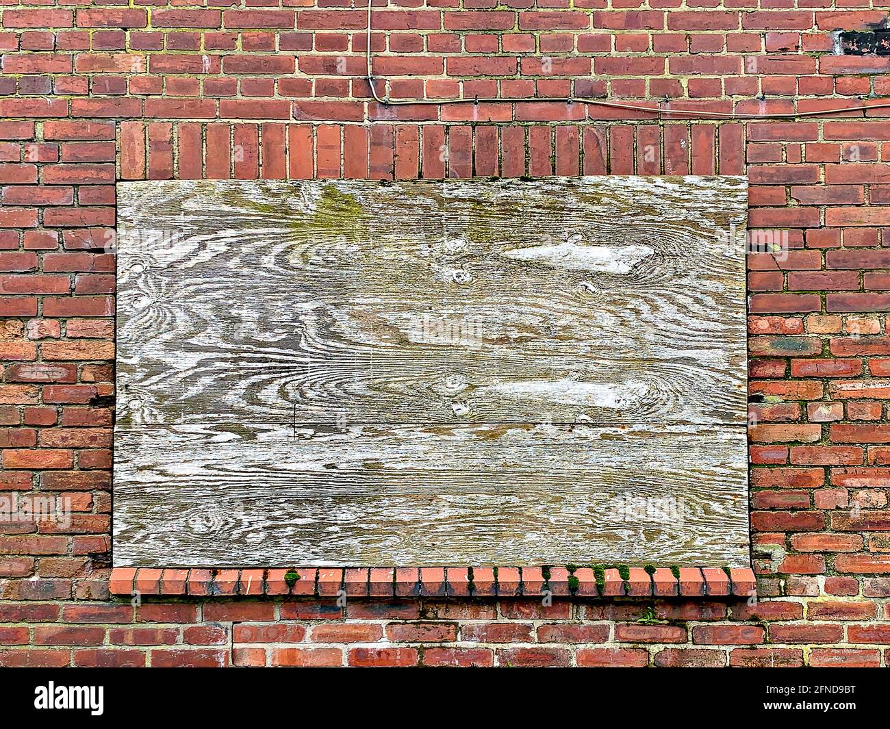 Stilles Fenster in Ziegelwand mit Sperrholzplatte bedeckt Stockfoto