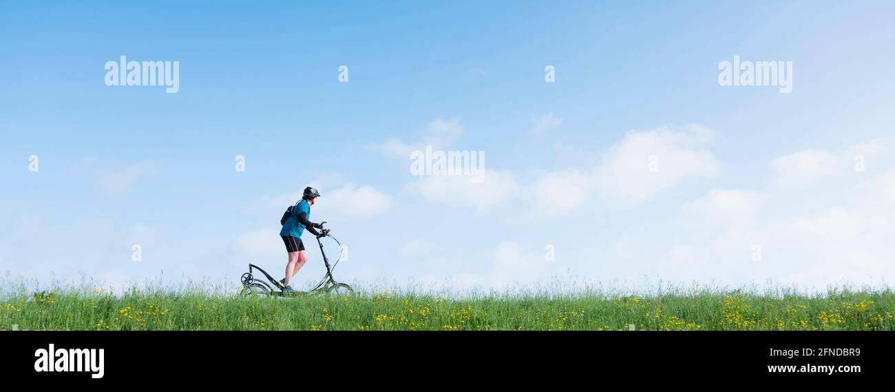 Frau fährt Elliptigo Bike auf grasbewachsenen Deich in holland unter Blauer Himmel Stockfoto