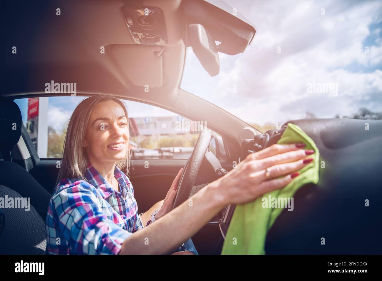 Lächelnde Frau verwendet ein Mikrofasertuch, um den Innenraum des Autos zu reinigen. Stockfoto