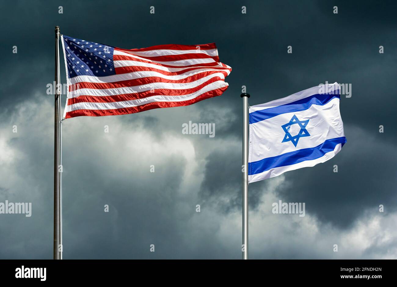 Staatsflaggen der USA und Israels flattern vor einem dunklen, stürmischen Himmel, symbolisches Bild für die Partnerschaft zwischen Israel und den USA in schwierigen Zeiten Stockfoto