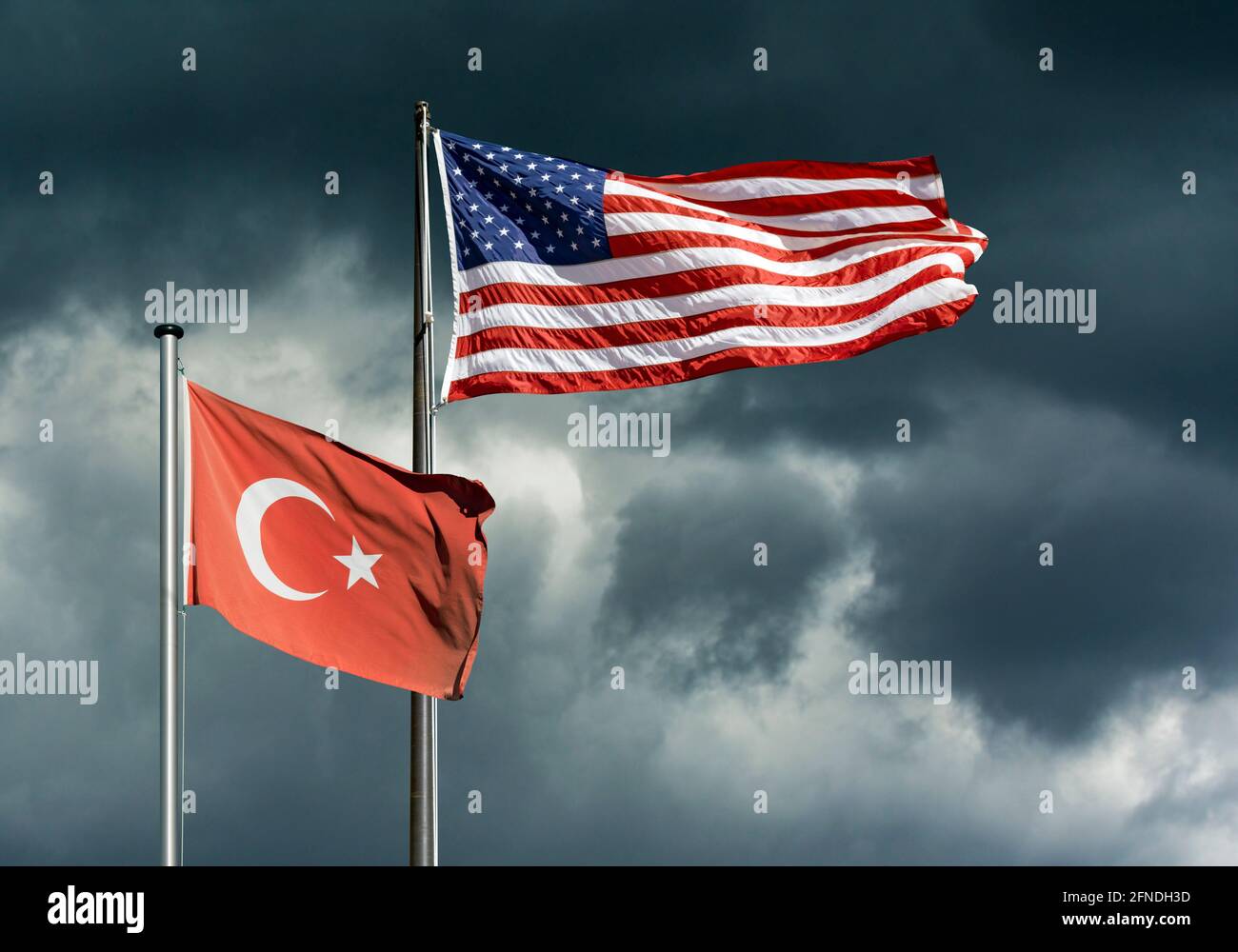 Staatsflaggen der USA und der Türkei flattern vor einem dunklen, stürmischen Himmel, symbolisches Bild für schwierige politische Beziehungen zwischen den USA und der Türkei Stockfoto