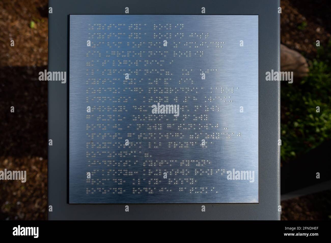 Beispieltext in Brailleschrift auf einer Informationstafel des Parks. Das Foto wurde bei natürlichem Tageslicht aufgenommen. Stockfoto
