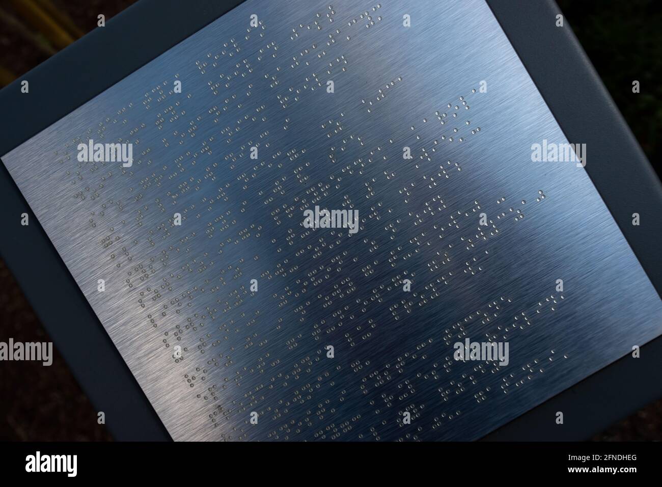 Beispieltext in Brailleschrift auf einer Informationstafel des Parks. Das Foto wurde bei natürlichem Tageslicht aufgenommen. Stockfoto