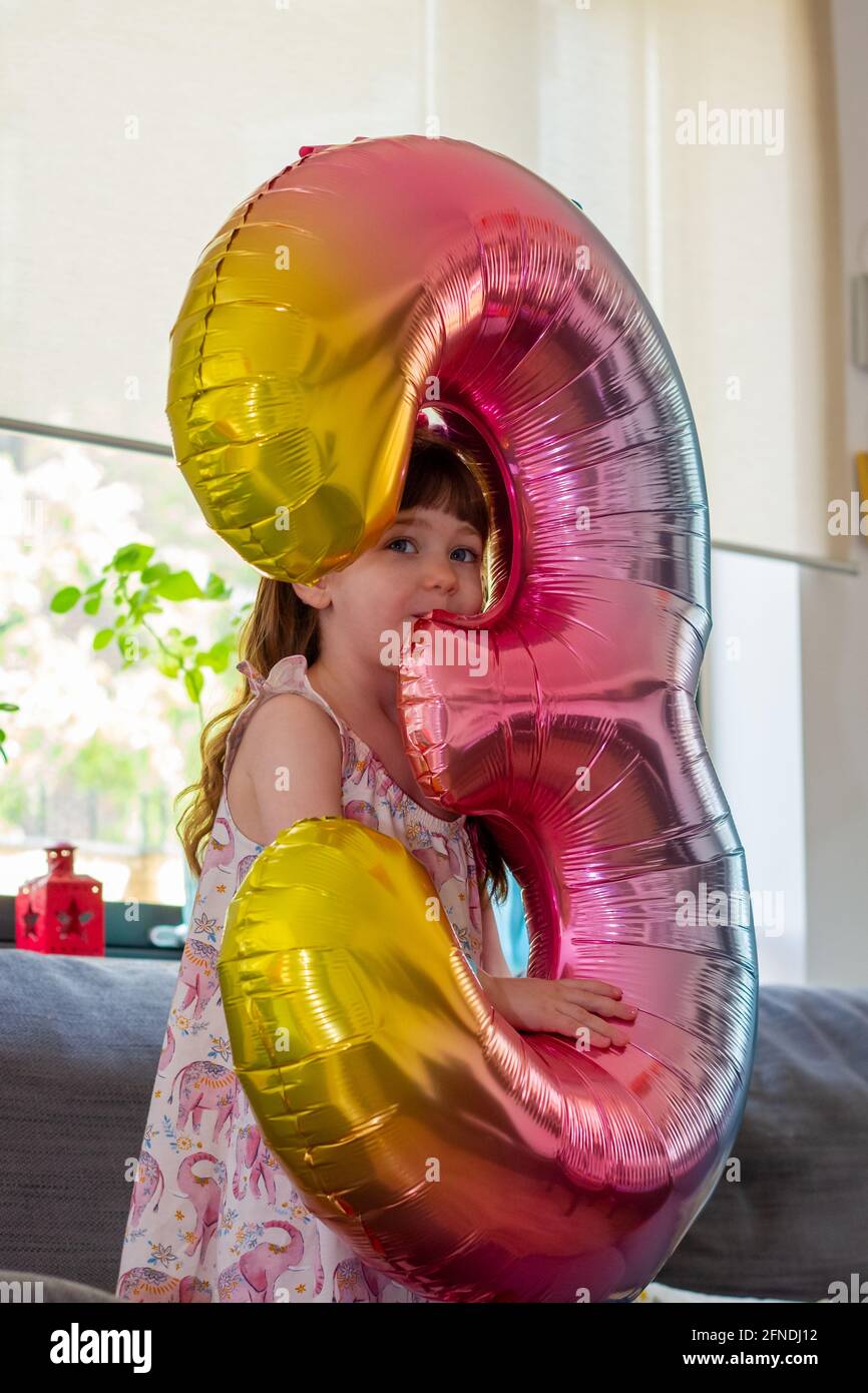 Porträt eines niedlichen, braunhaarigen Mädchens, das einen bunten Ballon der Nummer drei hält und die Kamera anlächelt Stockfoto