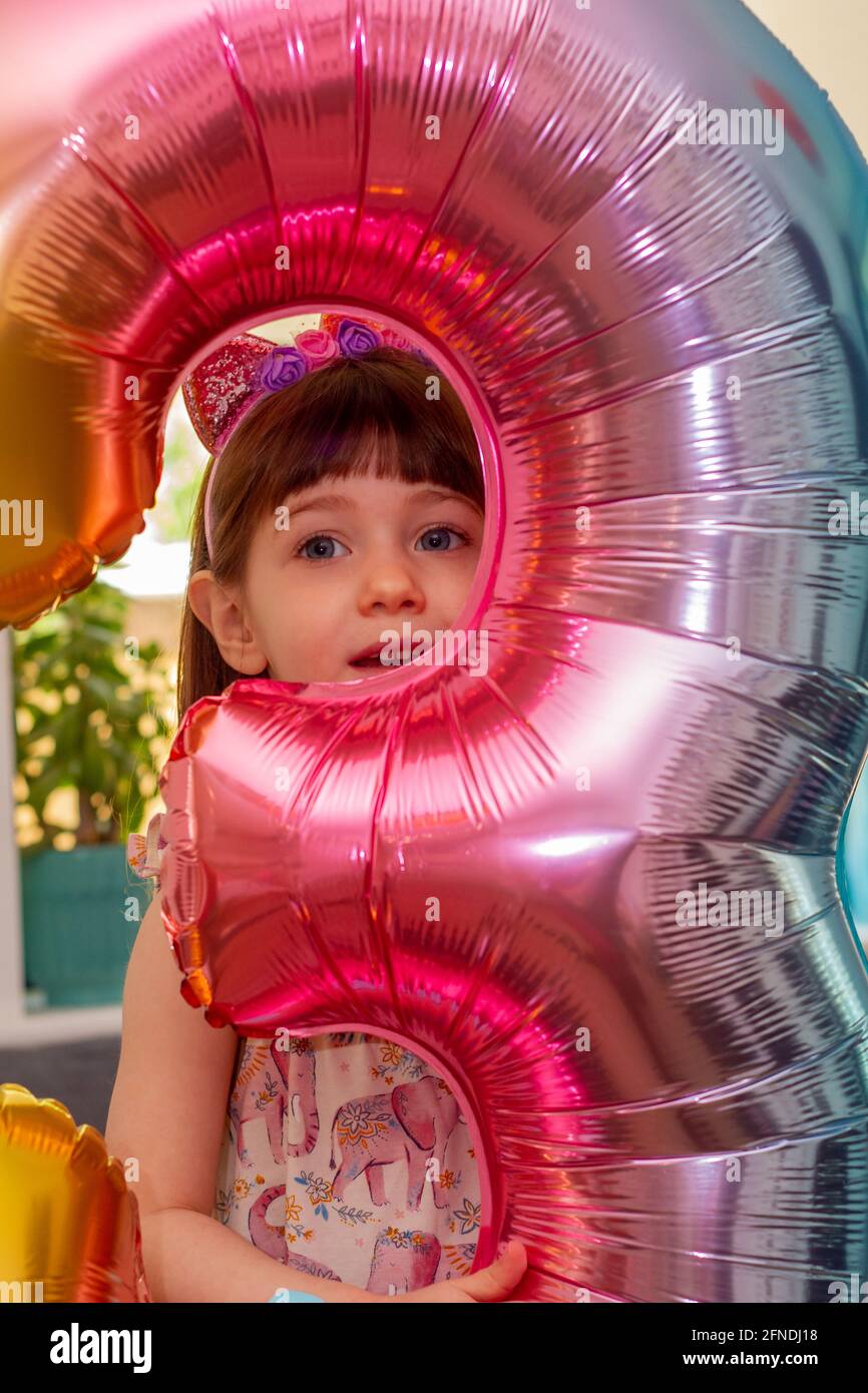 Porträt eines niedlichen, braunhaarigen Mädchens, das einen bunten Ballon der Nummer drei hält und die Kamera anlächelt Stockfoto