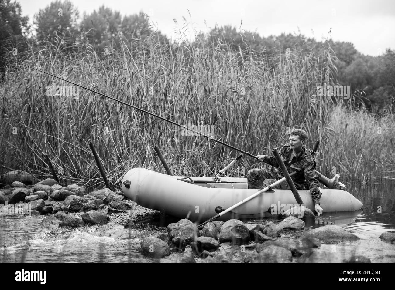 Blick auf eine Fischrute auf dem Fluss auf einem Gummiboot. Schwarzweiß-Foto. Stockfoto