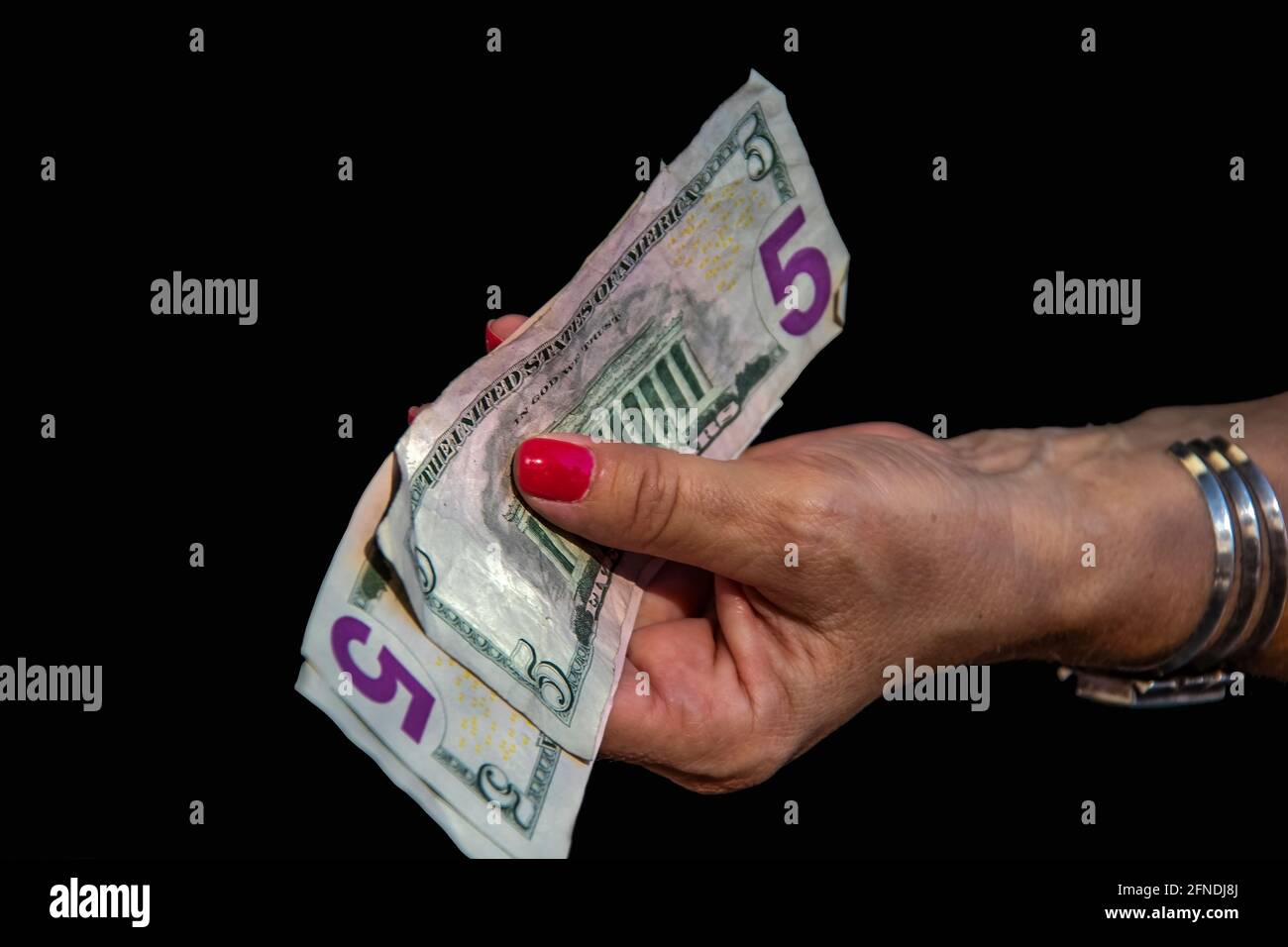 Frau mit Manschettenuhr und roten Fingernägeln hält mehrere fünf Der US-Dollar gibt den USD mit unlesbaren gelben Beschriungen aus Für etwas Abgeschiedenheit zu bezahlen Stockfoto