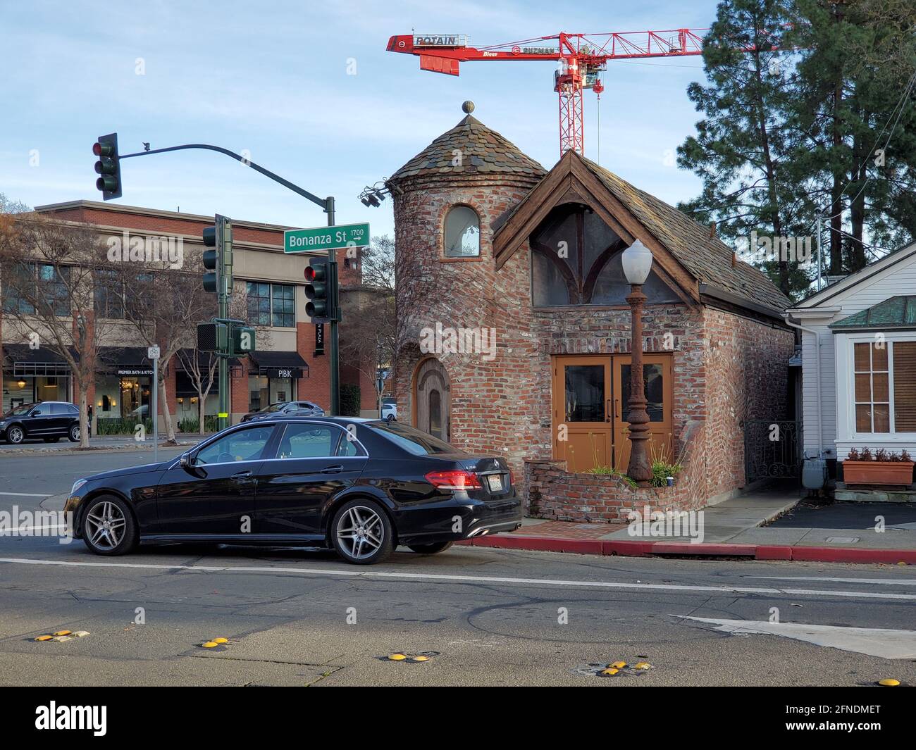 Weitaufnahme eines Mercedes Benz, der an einer Ampel an der Ecke der Bonanza Street wartet, mit einem turretierten Tudor Revival-Gebäude und einem hohen Kran im Hintergrund in Walnut Creek, Kalifornien, 9. Januar 2021. () Stockfoto