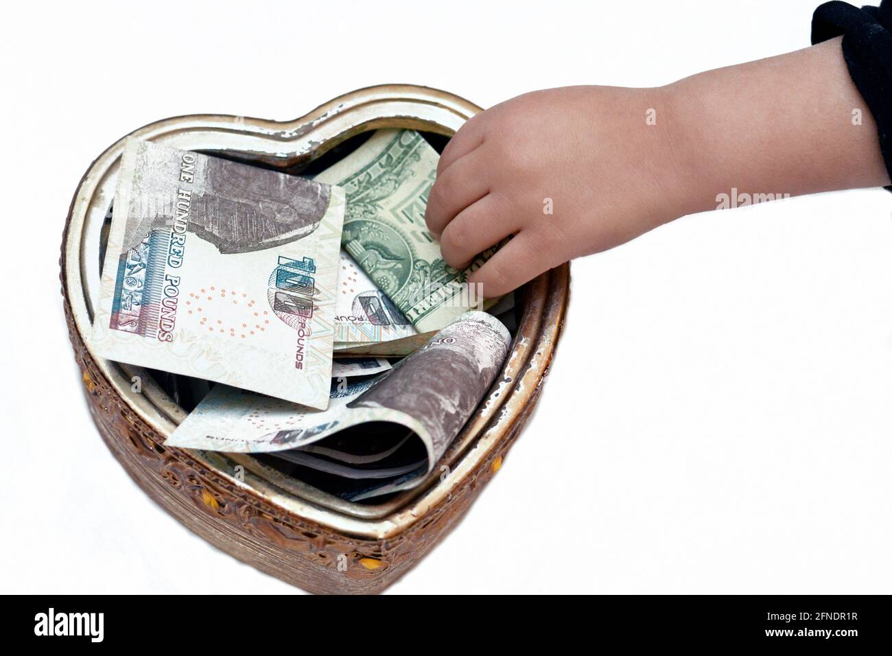 Ein Kind, das 1 Dollar in eine herzförmige Spendenbox steckt, Geld für wohltätige Zwecke sammelt, armen Menschen hilft, eine Schachtel mit mehreren Währungen, donat Stockfoto