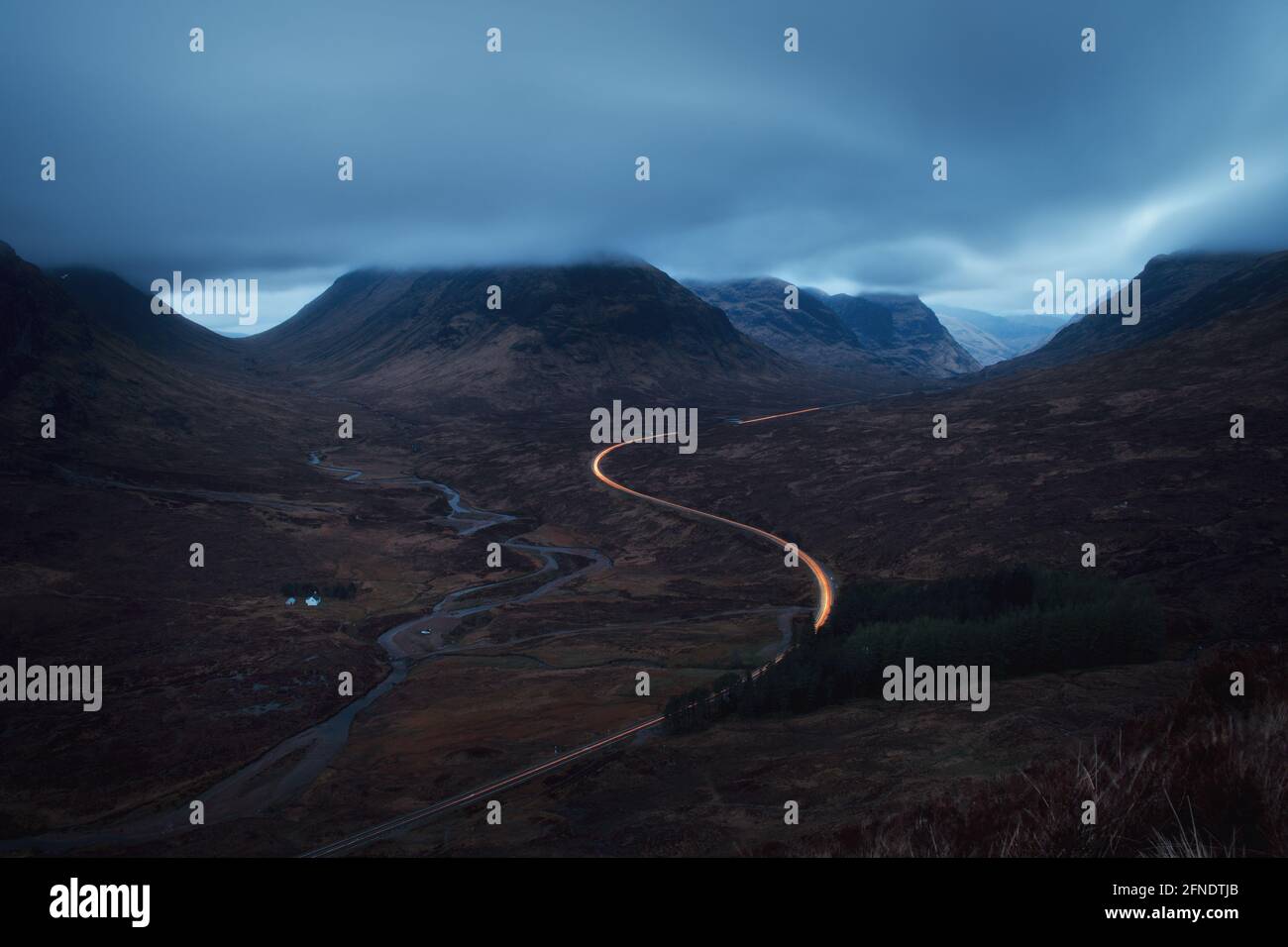 Morgenlandschaft mit Autoleuchten auf der Bergstraße, die nach Glencoe gegenüber von Buachaille Etive Mor führt. A82 Straße vor Sonnenaufgang. Schottland Stockfoto