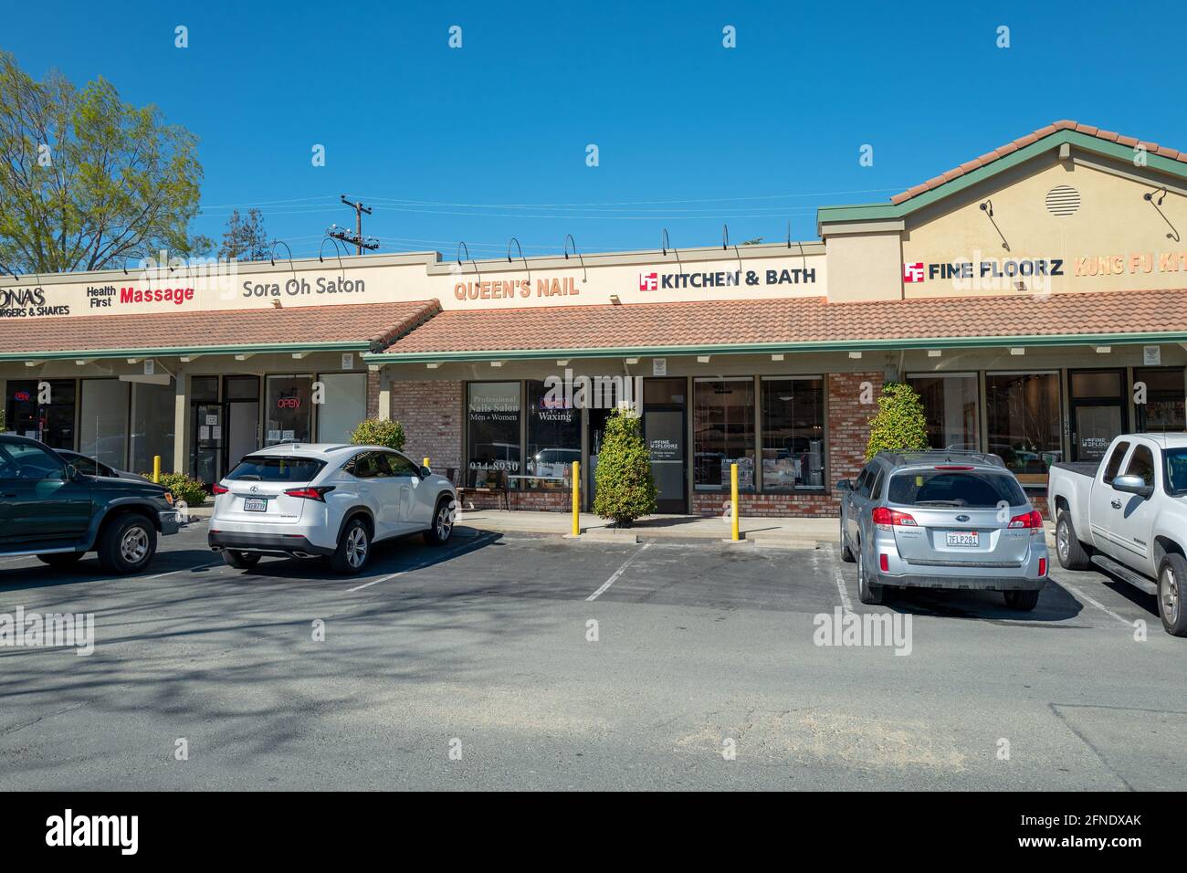Eine Vielzahl von Autos, die vor einem Einkaufszentrum mit mehreren Geschäften geparkt wurden, darunter Mona's Burgers and Shakes, Health First Massage, Sora Oh Salon, Queen's Nails und Fine Floorz, In Walnut Creek, Kalifornien, 17. Februar 2021. () Stockfoto
