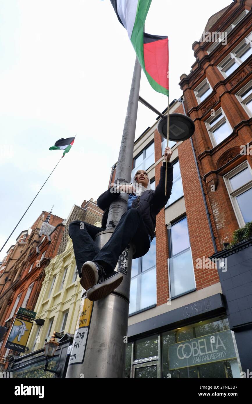 London, Großbritannien 15/05/21 EINE Frau klettert auf einen Lampenposten und schwenkt eine Flagge bei einer pro-palästinensischen Kundgebung in der Nähe der israelischen Botschaft, während die Spannungen zunehmen Stockfoto
