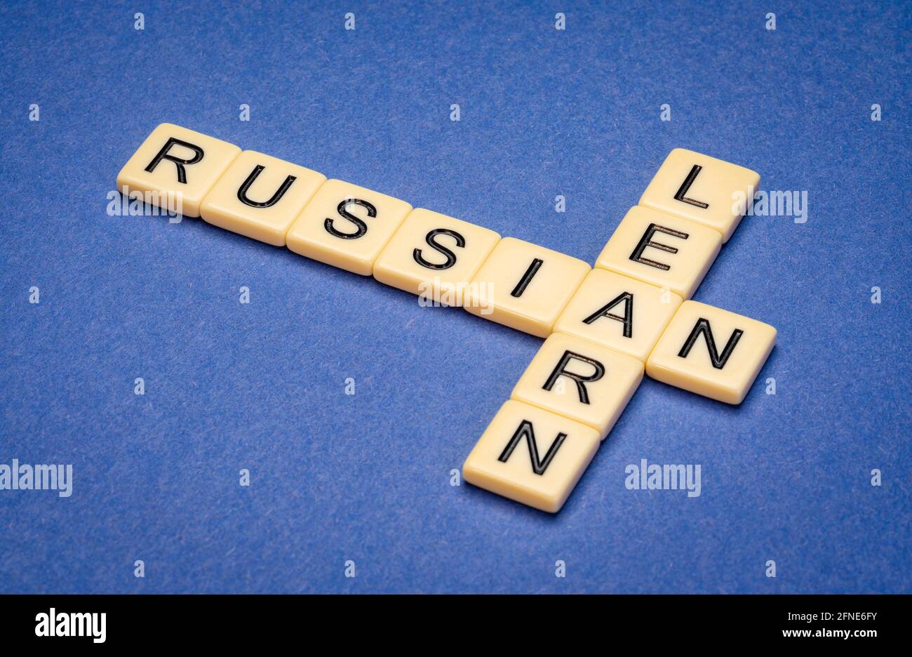 Lerne Russisch Kreuzworträtsel in Elfenbein-Buchstabenkacheln gegen blau strukturiert Papier Stockfoto