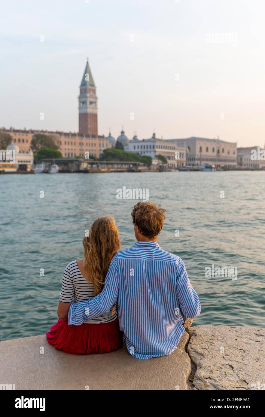 Das junge Paar sitzt am Meer und genießt den Blick auf den Markusplatz mit dem Campanile di San Marco, Venedig, Venetien, Italien Stockfoto