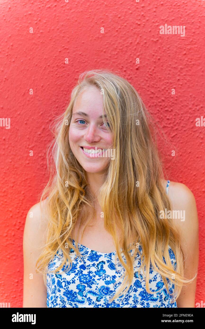 Porträt einer jungen Frau mit langem blondem Haar vor einer roten Mauer, lachend, Burano Island, Venedig, Venetien, Italien Stockfoto