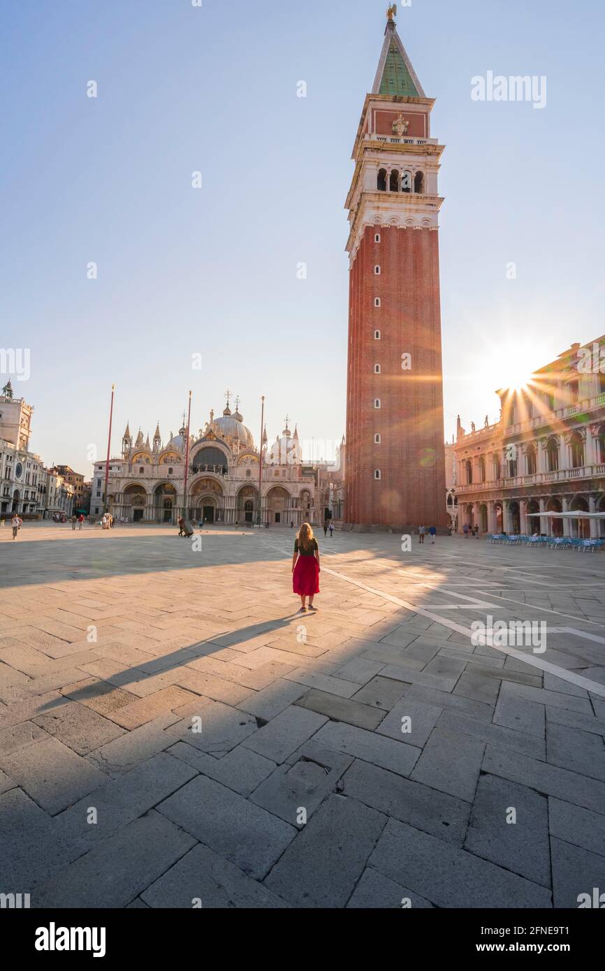 Junge Frau, Tourist mit rotem Kleid am Markusplatz, Sonne scheint auf dem Markusplatz mit Campanile di San Marco, Venedig, Venetien, Italien Stockfoto