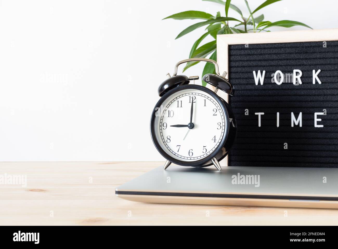 Klassischer schwarzer Vintage-Wecker, Laptop, Topfpflanze und Schild „Work  Time“ auf Holzschreibtisch mit weißem Wandhintergrund und Platz zum  Kopieren von Text Stockfotografie - Alamy