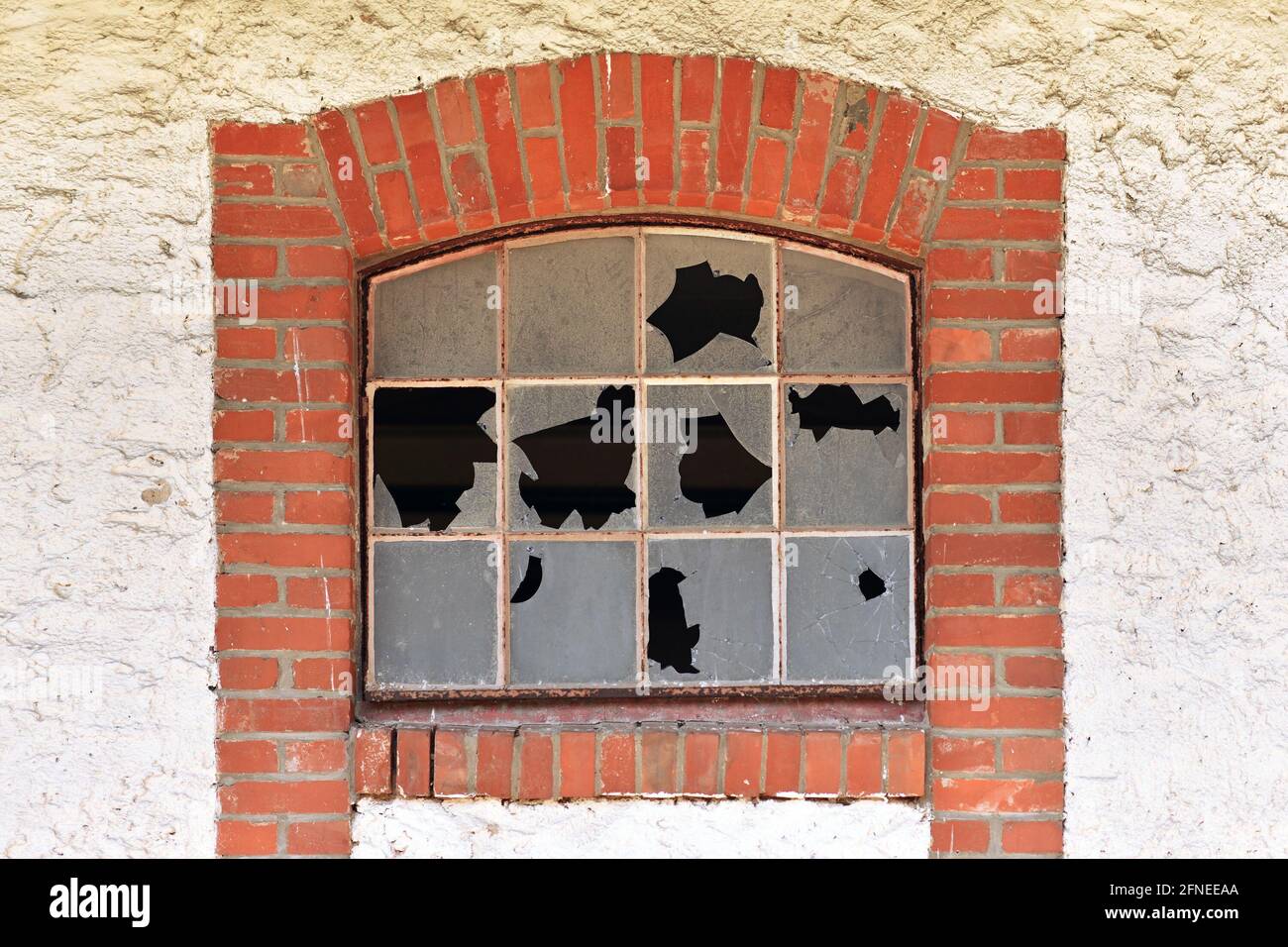 Kaputtes Blechfenster mit zerbrochenem Glas eines alten verlassenen Gebäudes Mit rotem Backsteinrahmen Stockfoto