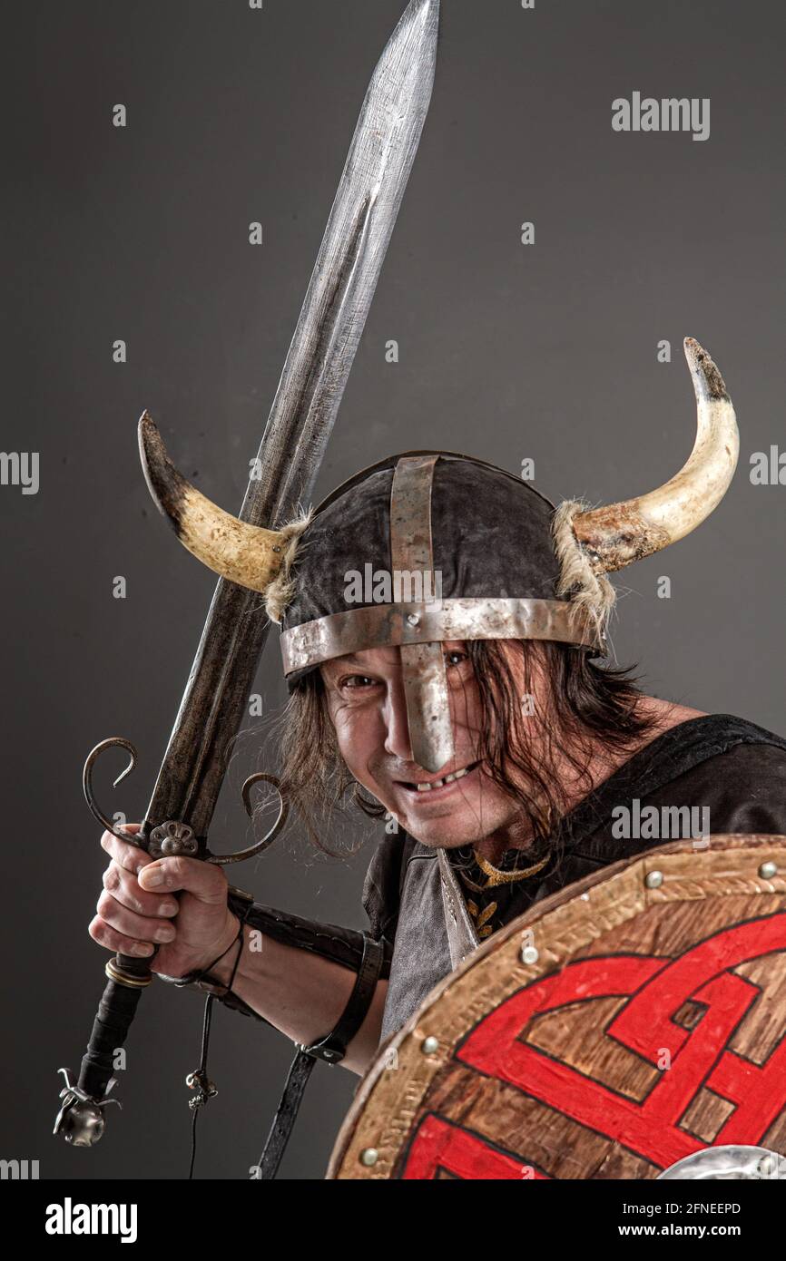 Komischer Ritter in einem gehörnten Helm mit einem Schild und Schwert auf dunklem Hintergrund Stockfoto