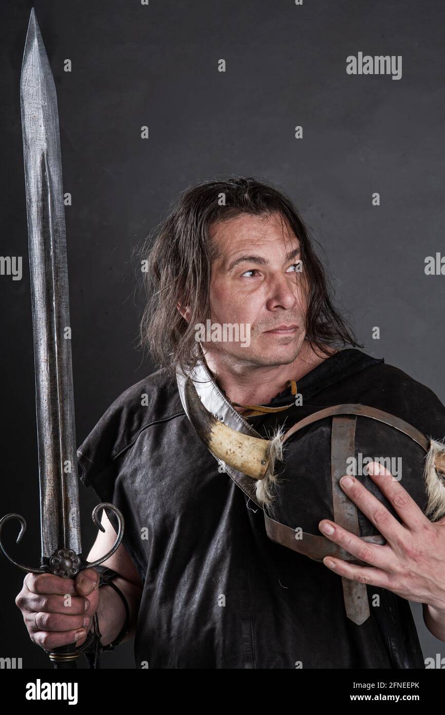 ritter hält einen gehörnten Helm und ein Schwert in seinem Hände auf dunklem Hintergrund Stockfoto