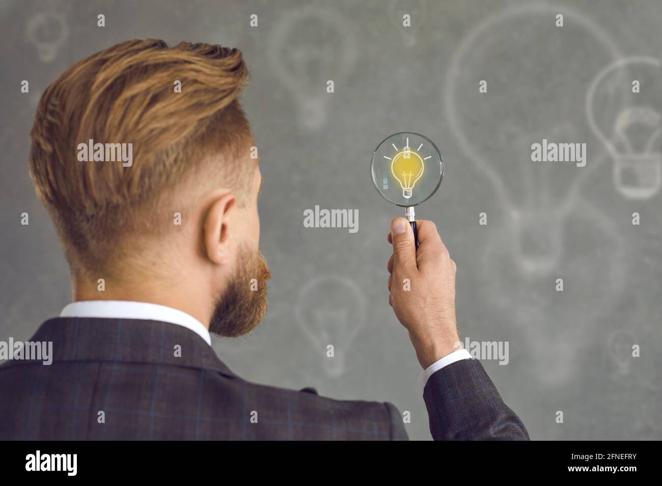 Mann mit Lupe Blick auf gelbe Glühbirne als Symbol der Geschäftsidee Stockfoto