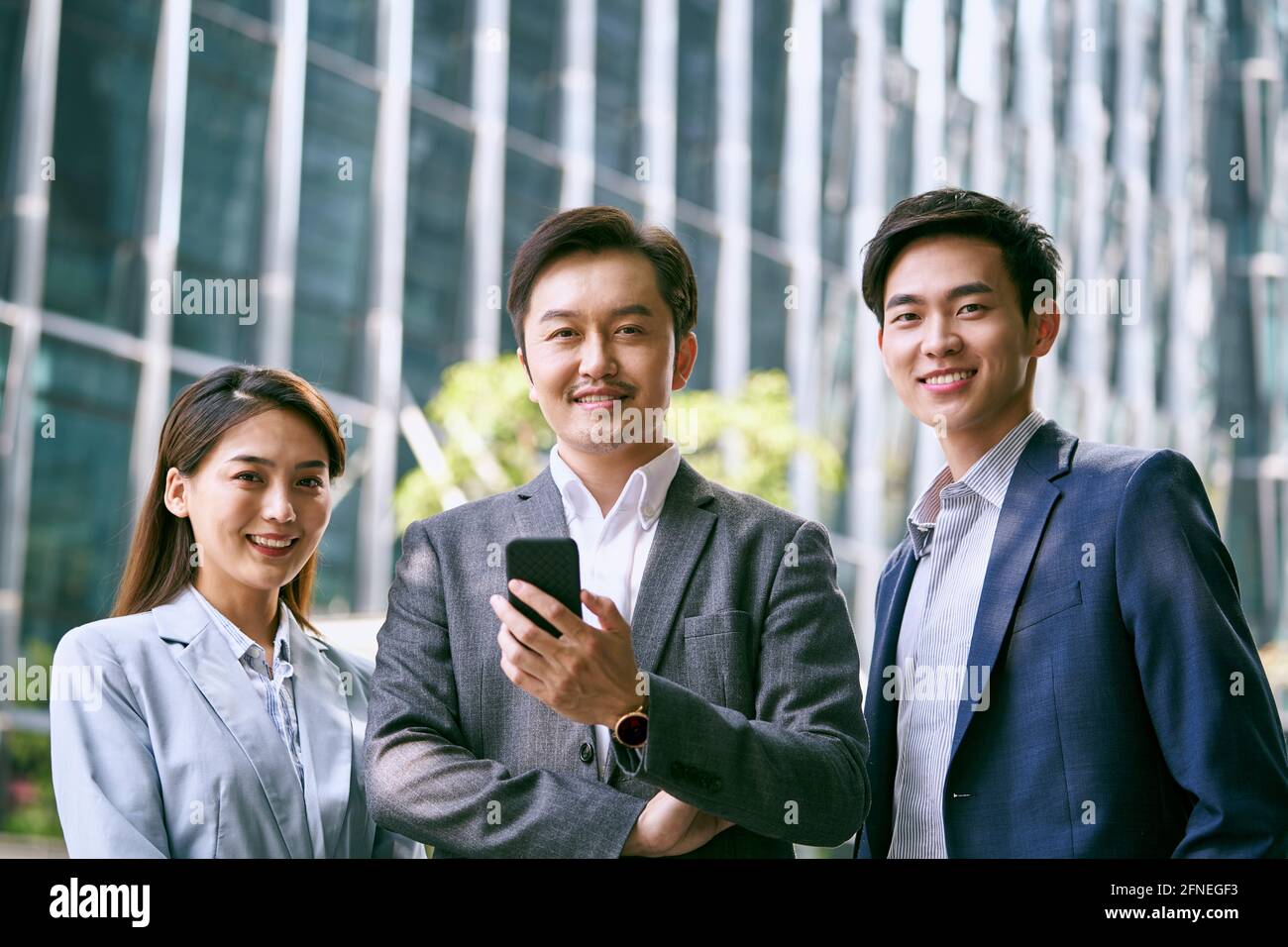 Außenportrait eines Teams aus drei asiatischen Geschäftsleuten, die auf der Suche sind Lächelnd vor der Kamera Stockfoto