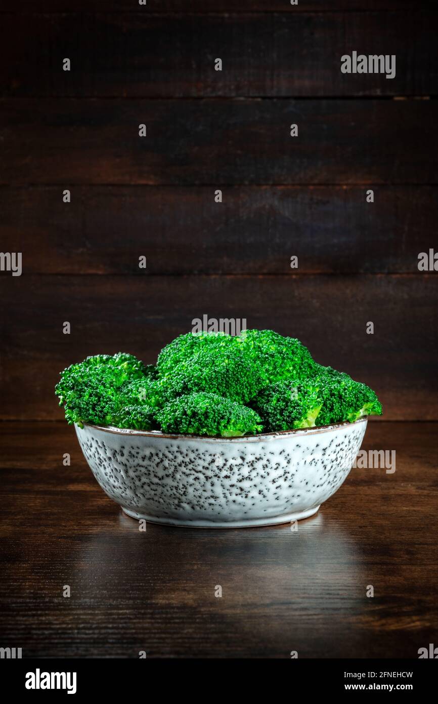 Gekochter Brokkoli in einer Schüssel, eine Seitenansicht auf einem dunklen rustikalen Holzhintergrund mit Kopierraum. Grünes Gemüse Detox Mahlzeit Stockfoto
