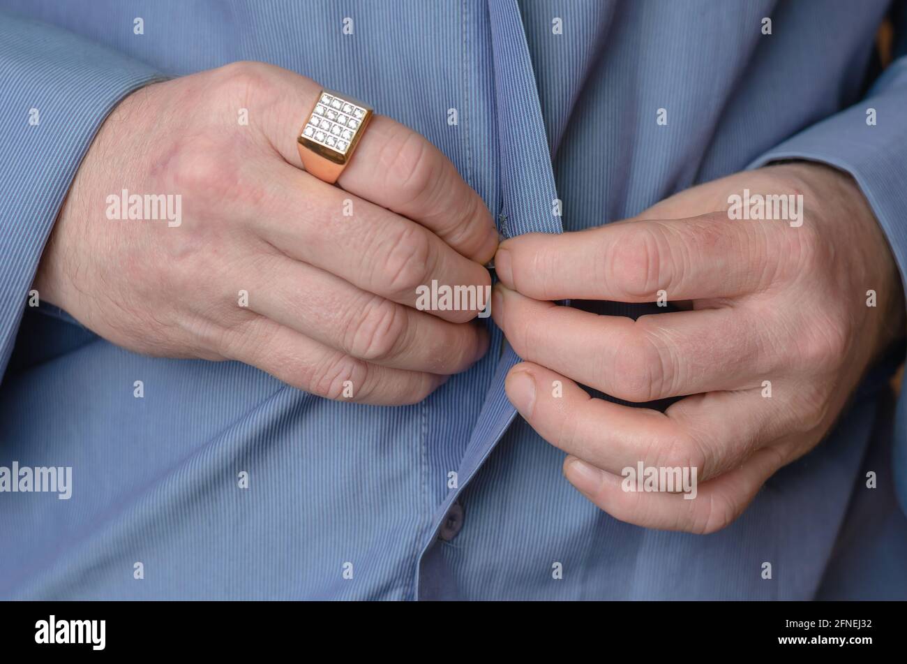 Nahaufnahme seiner Hände, die den Knopf auf seinem blauen Hemd drücken. Ein  erwachsener Mann mittleren Alters mit einem goldenen Ring an seinem  Zeigefinger. Person, die die Hände in Meilen hält Stockfotografie -